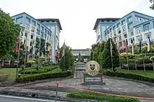 Photographie de deux bâtiments identiques se faisant face. Au milieu d'eux se trouve une place entourée de drapeaux du monde entier et au centre de laquelle se trouve le blason des Universités Malaisiennes de Sabah, en-dessous duquel se trouve l'inscription « Laman Canselori ».