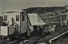 Marie Krogh procède à des mesures ou à des réglages sur un appareil relié à une cabine fermée installée dans la toundra du Groenland.