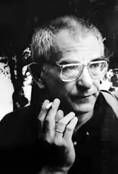 Photo en noir et blanc d'un homme avec de grandes lunettes fumant une cigarette.