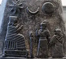 Sculpture d'un roi parlant à deux personnes. Au-dessus de lui une étoile, un croissant et un cercle.