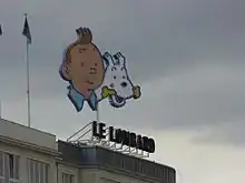 Visages de Tintin et Milou (tenant un os dans la gueule) au-dessus du toit d'un immeuble.