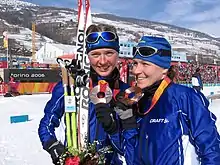 Deux athlètes, de face, avec bonnet et lunettes sur la tête, posant devant avec leurs médailles devant les photographes.