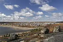 Un village de quelques centaines de maisons est bordé par une plage sablonneuse et une rivière. La végétation se limite à quelques mousses. Trois grosses pierres sont en évidence à l'avant-plan.