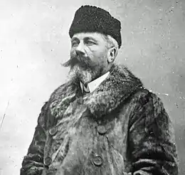 Portrait en buste d'un homme de trois-quarts vêtu d'un manteau d'hiver avec une moustache et un bouc fournis.