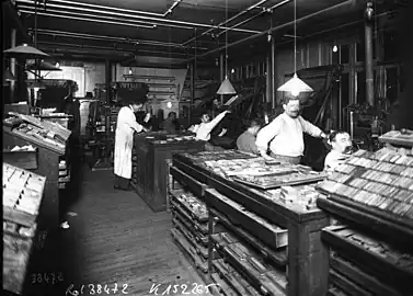 Photographie en noir et blanc d'ouvriers travaillant à la création d'un journal papier au début du XXème siècle.