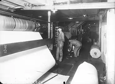 Photographie en noir et blanc d'ouvriers travaillant à la création d'un journal papier au début du XXème siècle.