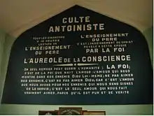 Grand panneau de couleur vert foncé sur lequel est écrit L'Auréole de la Conscience en majuscules, au-dessus de la tribune, à l'intérieur d'un temple