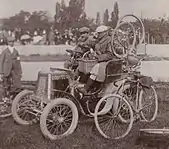 Photographie en noire et blanc d'une automobile pilotée par deux hommes.