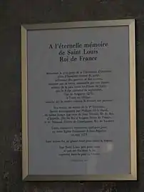 Panneau encadré posé sur un mur de pierre, et dont le titre est « À l'éternelle mémoire de Saint Louis, Roi de France »