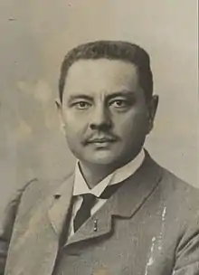 Portrait d'un homme moustachu portant un costume et une cravate.