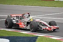 Photographie d'une monoplace de Formule grise et rouge, vue de trois-quarts, près d'un vibreur.