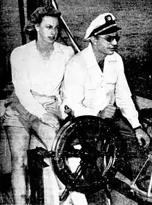 Hubbard, devant avec des lunettes de soleil et une casquette et Sara, derrière en short. Les 2 tenant la barre.