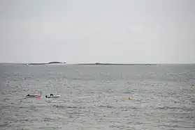 Vue en couleur d'une île plate en arrière plan d'une étendue d'eau, montrant deux barques.