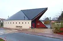 Photographie en couleurs d'un bâtiment récent dont l'architecture présente un toit en forme d'auvent très avancé.