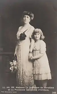 En tenue d'apparat claire, Henriette, coiffée d'un imposant chignon et tenant un éventail dans sa main droite, pose debout avec sa fille, souriante, à laquelle elle tient la main