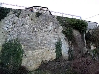 En contrebas de l'église dont on aperçoit une partie du chevet, la falaise est maintenue par un haut mur percé par un escalier raide et étroit que l'on remarque à droite.