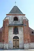 La façade en pierre calcaire soutenue par des contreforts en brique sur lesquels est écrite, en briques vernissées, la date de reconstruction : 1-7-8-1.