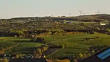 Des collines couvertes de boisés et de champs cultivées, ponctuées de bâtiments de ferme et d'éoliennes.