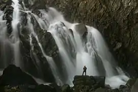 Vue de l'intérieur d'une grotte, avec un homme devant une cascade d'eau.