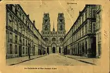 Rue avec deux séries de bâtiments homogènes de chaque côté, donnant sur la façade de la cathédrale et ses deux tours.