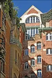 Photo en couleur deux deux façades de brique en angle rentrant avec encorbellements à gauche et fenêtres en escalier au fond