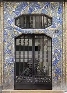 Photographie d'une porte d'entrée d'immeuble entourée de mosaïques bleues et or.