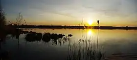 Le crépuscule sur le Lac de Bordeaux. En avant plan, le soleil se reflète dans l'eau, lui donnant des couleurs jaunes et orange.