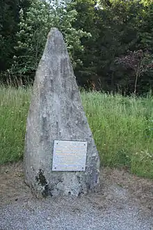 photo couleur d'une pierre de granite brute dressée. Un plaque de granite polie porte un texte.