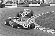Photographie en noir et blanc de deux monoplaces de Formule 1 dans un virage.
