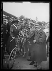 Photographie en noir et blanc d'un coureur recevant un bouquet de fleurs et entouré par la foule.
