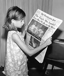 Une jeune fille tient un journal à la main.
