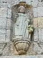 Statue de saint Méen tenant un chien muselé.