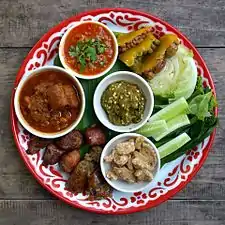 Un échantillon de la cuisine du nord de la Thaïlande (Lanna). En commençant par le haut : nam phrik ong, à gauche le kaeng hangle, au milieu le nam phrik num (purée de piments verts grillés, échalotes et ail), en dessous un petit bol de kaep mu (couennes de porc frites), avec à gauche des tranches de sai ua (saucisse de porc épicée grillée) et de si khrong mu thot (morceaux de côtes de porc frites).