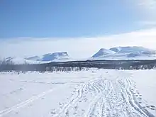 collines enneigées et ensolleillées, à l'horizon une trouée dans le relief forme une porte, quelques traces de ski.