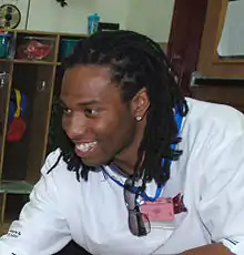 Larry Fitzgerald, un homme noir, avec des tresses, un t-shirt blanc et une boucle d'oreille, sourit à des supporters.