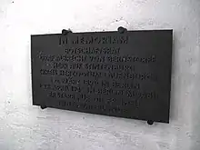 photographie d'une plaque noire gravée, fixée sur un mur blanc.