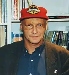 Photo d'un homme devant une bibliothèque, avec une casquette rouge