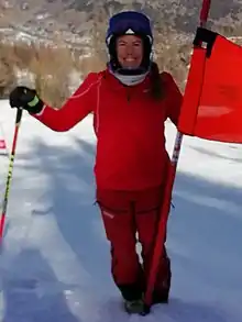 Laurie Mougel dans la tenue rouge de l'ESF, debout au portillon de départ à côté d'une porte rouge de Géant.