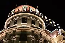 Vue en contre-plongée de nuit du haut d'un palais sur lequel on voit en majuscules électrifiées « Le Negresco ».