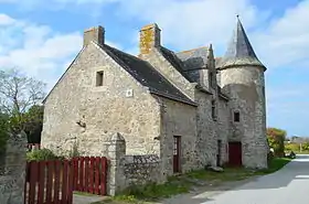 Vue d'un manoir en granit avec une tourelle coiffée d'un toit conique.