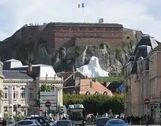 photographie la statue du Lion de Belfort bâchée avant son inauguration avec au premier plan la Vieille Ville et à l'arrière-plan la citadelle et sa caserne.