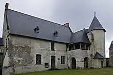 Photographie en couleurs de la façade bâtiment à toit pentu accolé d'une galerie en hauteur et d'une tourelle octogonale sur la droite.