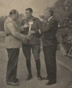 Antonin Magne en uniforme entre deux journalistes en civil, qui lui tendent une louche.