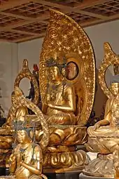 Photo couleur de statues en bois laqué et doré de divinités bouddhiques dans une salle d'un musée.