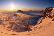 Soleil de fin d'après-midi d'hiver éclairant un monolithe rocheux, avec un sommet dépassant d'une mer de nuages en arrière-plan.