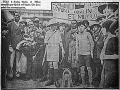 Photographie extraite d'un journal et montrant un jeune garçon accompagné d'un chien et entouré d'une foule nombreuse.