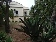 Parc botanique avec cactées au premier plan. Maison de maître dans le fonds avec fronton d'architecture néopalladienne.