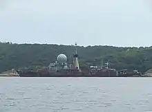 Photographie couleur d'un navire embossé, portant un gros râdome et une cheminée conséquente.
