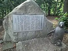 Photographie couleur d'une stèle en pierre avec une plaque commémorative et une petite sculpture de manchot.