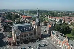 Photographie en couleur représentant, au premier plan, une vue surplombante de l'hôtel de ville et, au second plan, une rivière en haut à gauche et un pont à droite